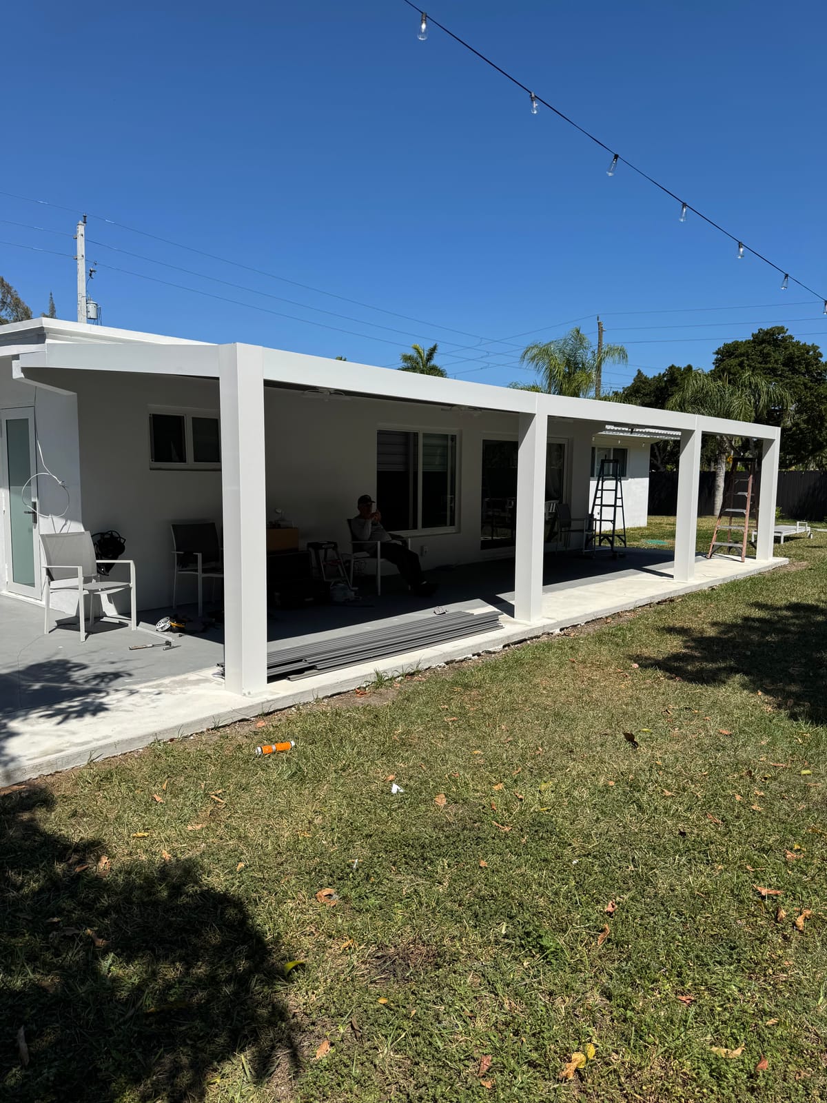 Aluminum pergola beams along the back of a South Florida home, strung with string lights over the patio