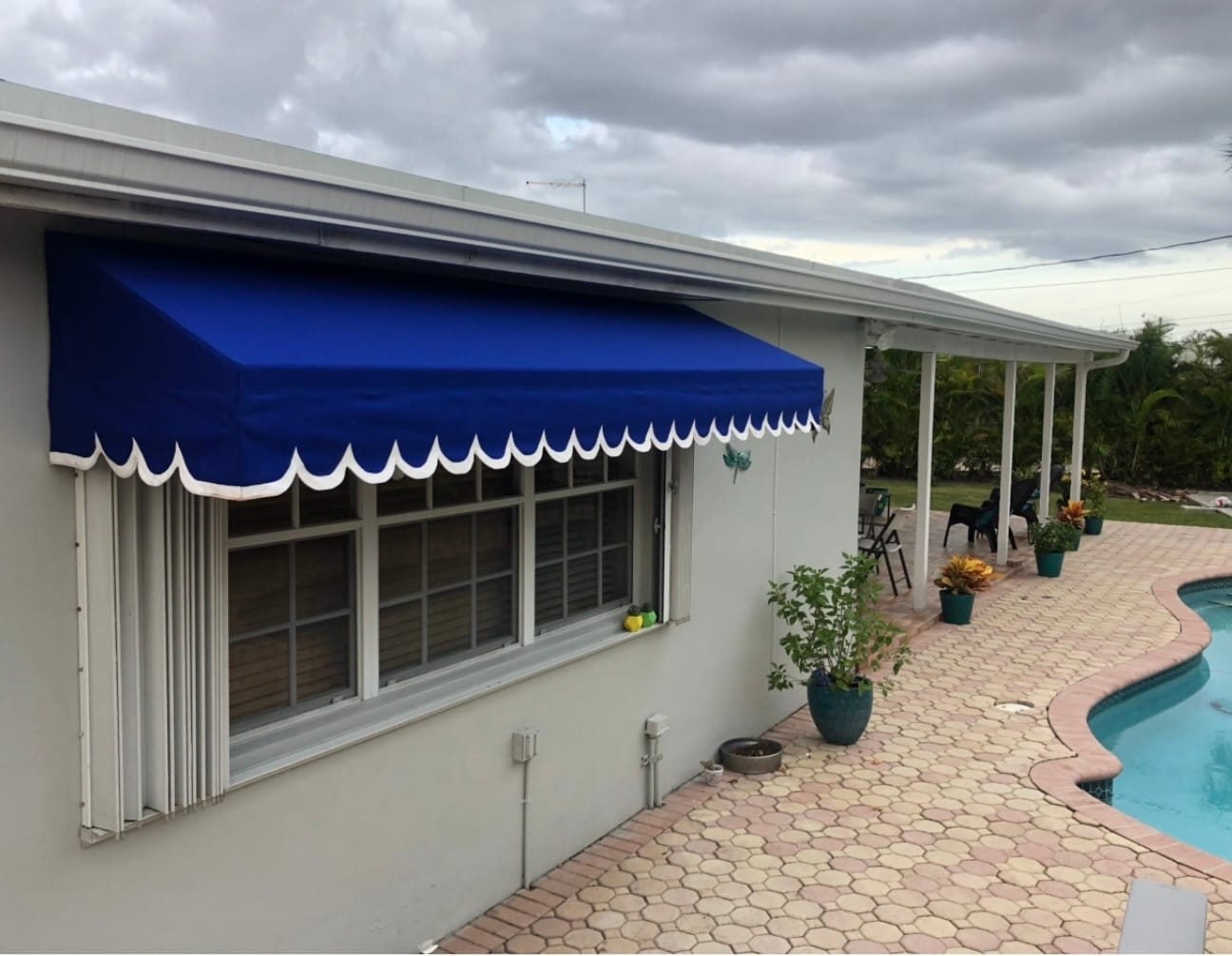 Blue fabric window awning with scalloped white trim beside a swimming pool in Miami